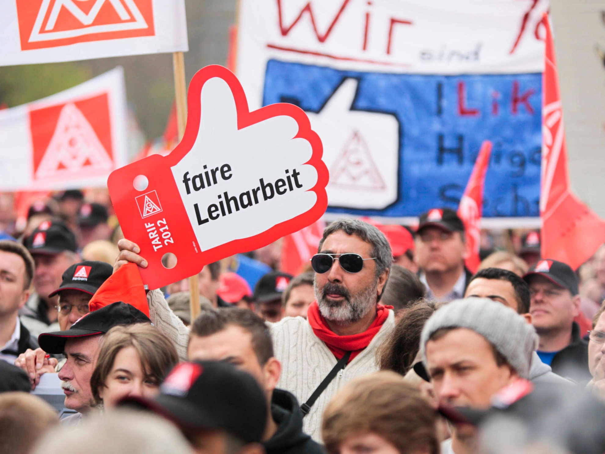 Ein Mann mit Sonnenbrille hält bei einer Demonstration ein Schild mit der Aufschrift: Faire Leiharbeit